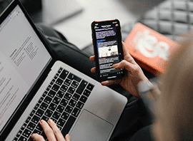 Person multitasking with a laptop and smartphone, reading online content.