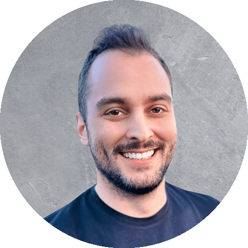 Batu, a professional speaker with short dark hair, a well-groomed beard, and a friendly smile, wearing a black t-shirt, in front of a textured gray background.